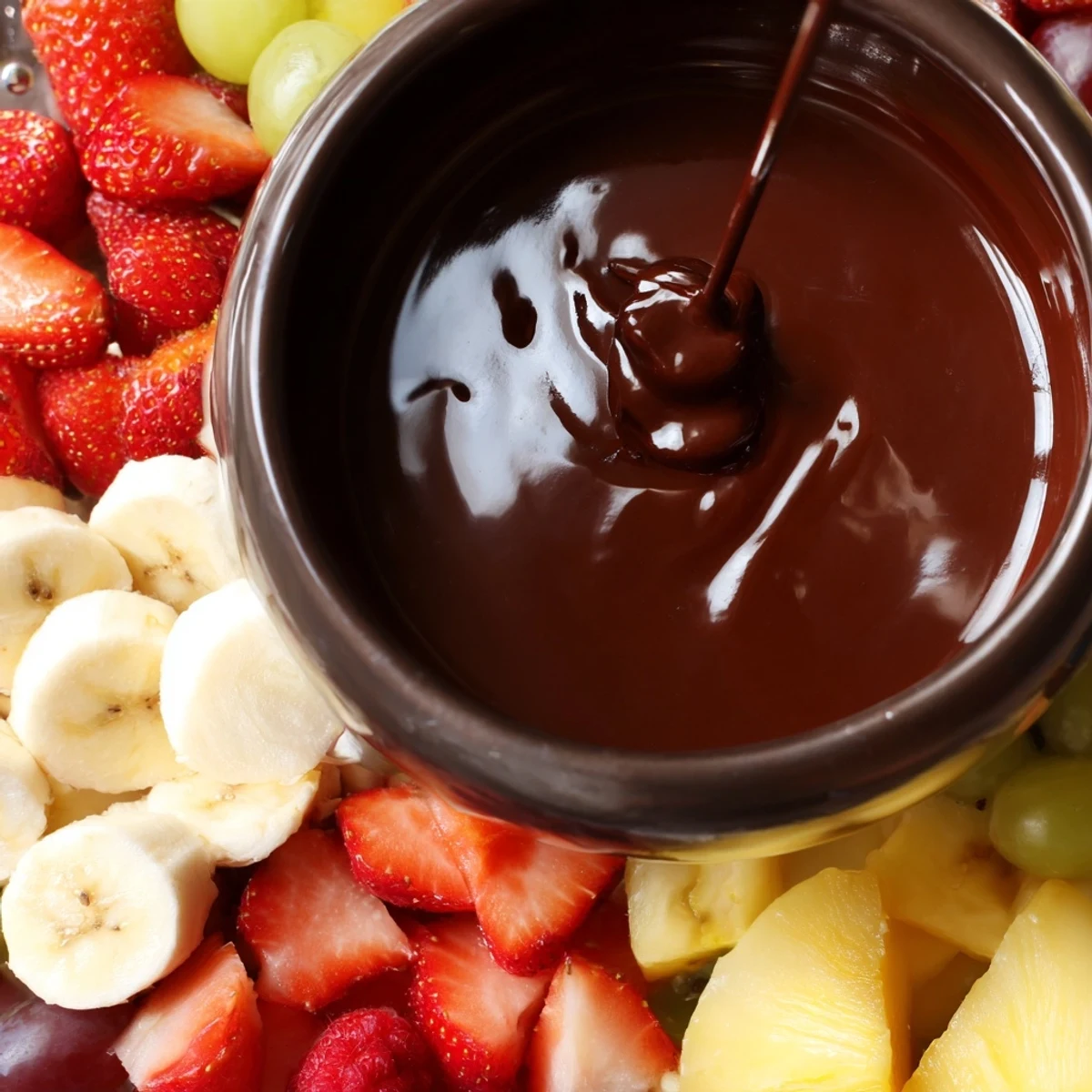 Indulgent chocolate fondue swirl and fresh fruit for dipping, served with apple slices, grapes, and kiwi.