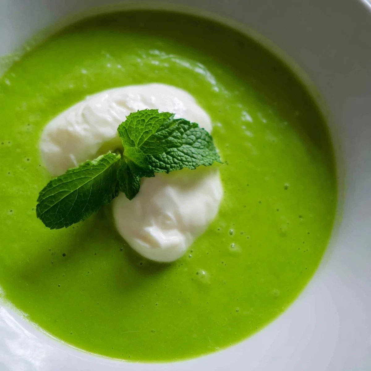 Ladle of velvety Green Pea and Mint Soup garnished with a dollop of crème fraîche and cracked black pepper.