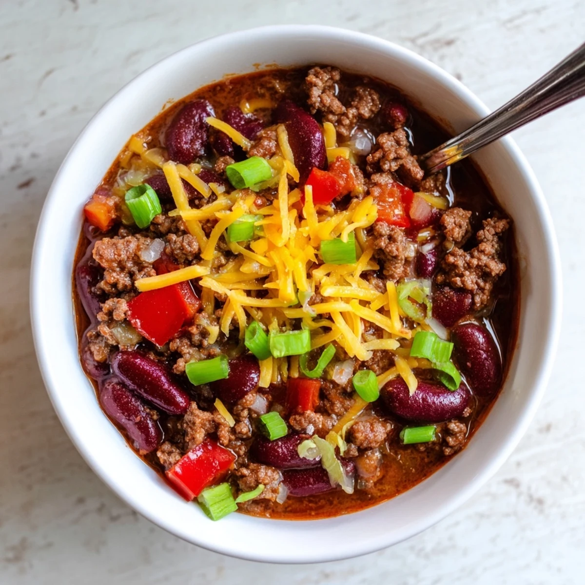 Steaming Beef and Bean Chili with cheddar cheese, served with tortilla chips and fresh lime wedges on the side.