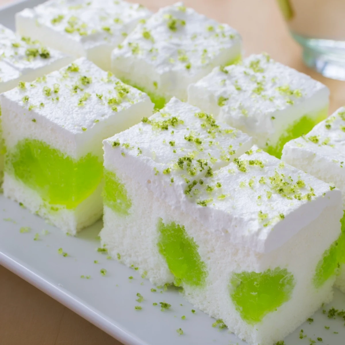 Chilled St. Patricks Day Lime Poke Cake slice held by a fork, revealing creamy lime filling and soft cake, garnished with green sprinkles for the holiday.