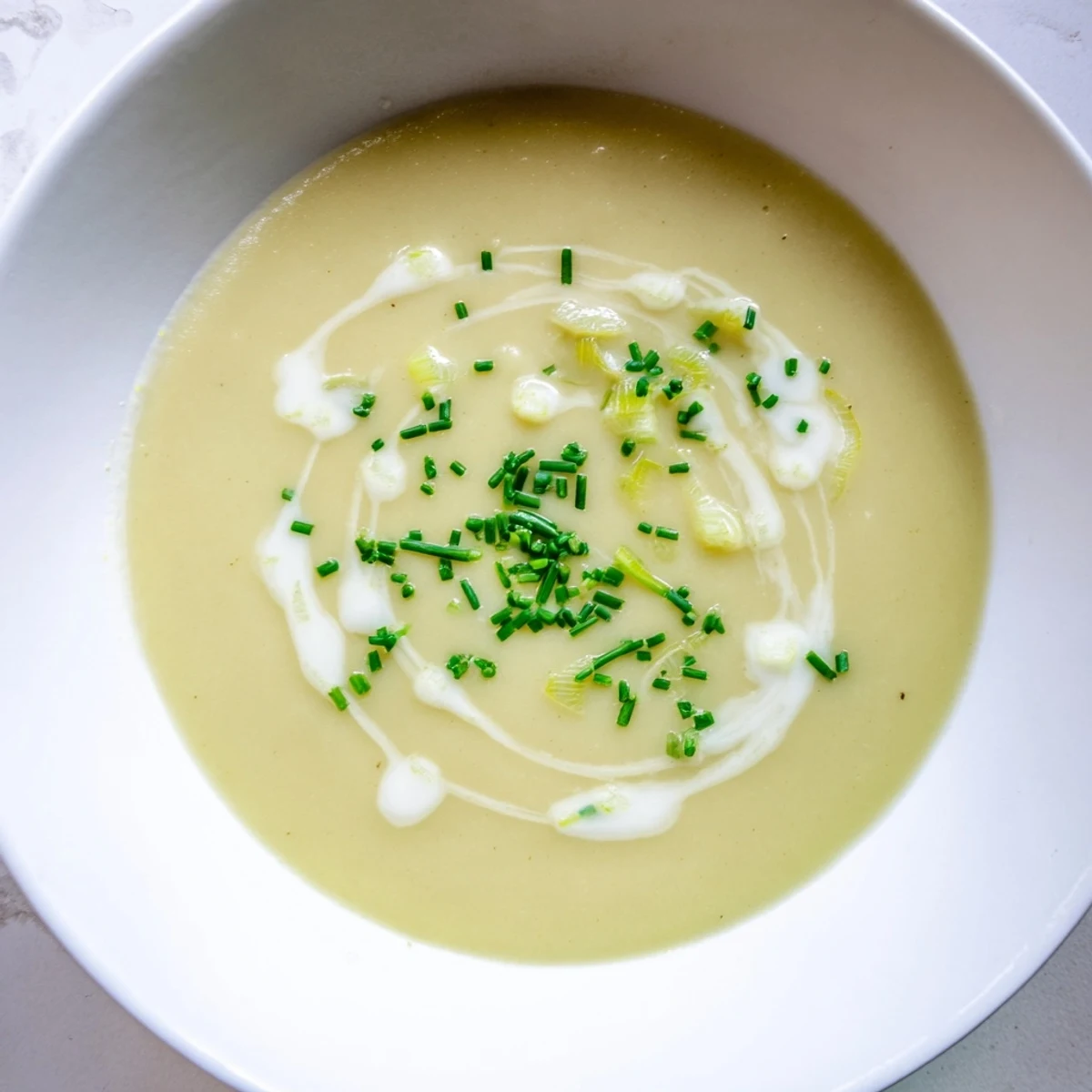 Creamy Leek and Potato Soup with Cream swirled in a rustic bowl, garnished with fresh chives and a drizzle of heavy cream.