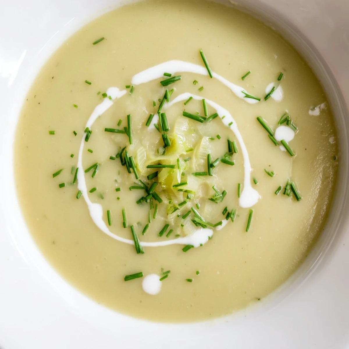 Smooth, comforting Leek and Potato Soup with Cream in a white ceramic bowl, with sliced leeks and a dollop of cream.