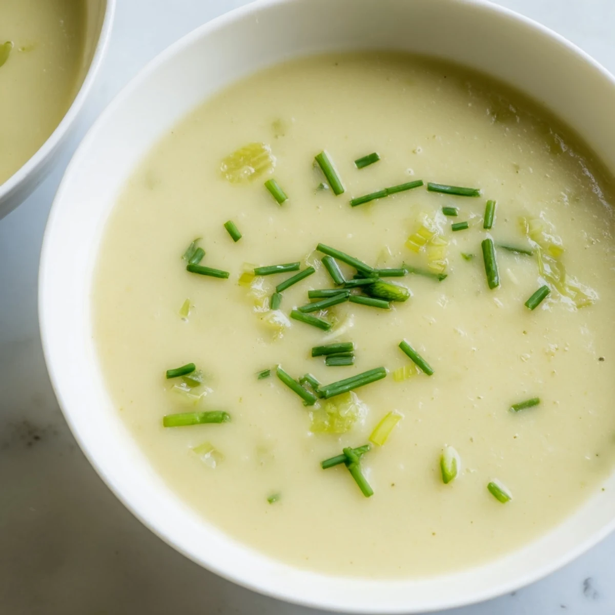 Creamy Leek and Potato Soup garnished with fresh chives in a white ceramic bowl with a rustic spoon.