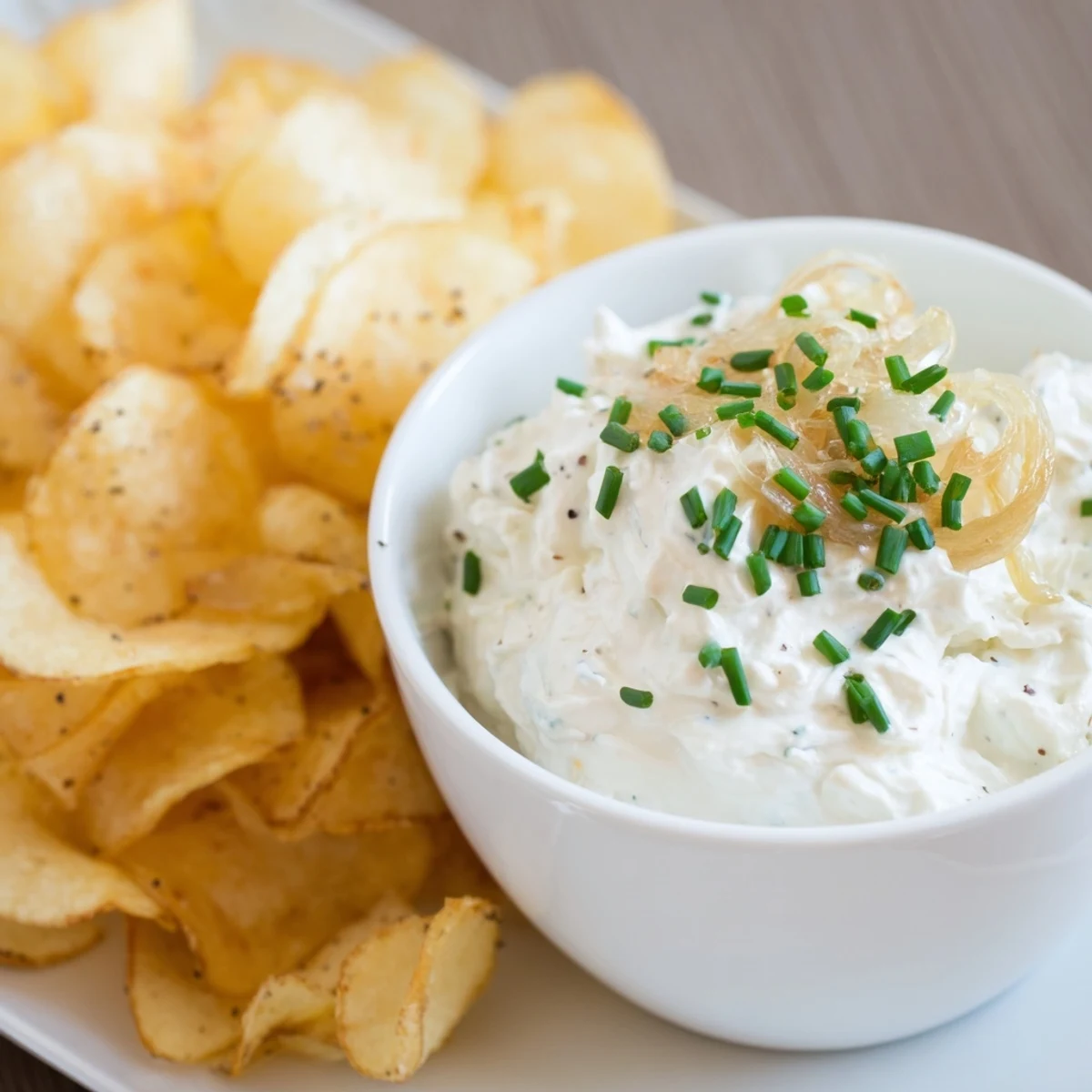 Freshly fried russet potato chips alongside a rich, homemade onion dip garnished with bright green chives.