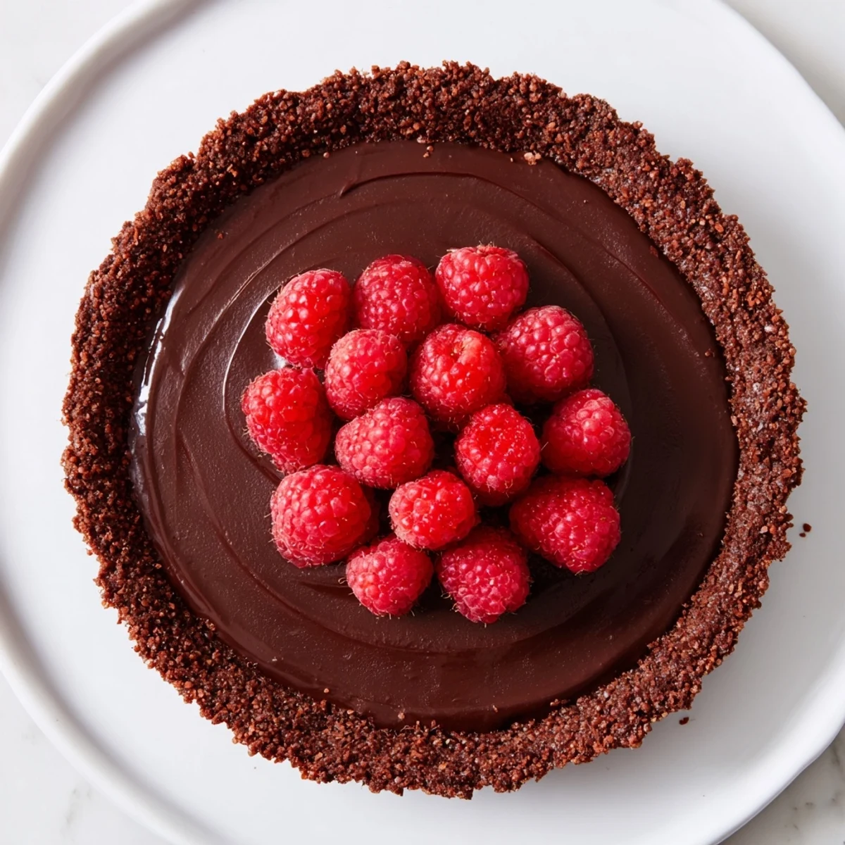 Freshly sliced chocolate raspberry tart on a white plate, topped with glossy, tart raspberries and a light dusting of powdered sugar for a perfect dessert presentation.  