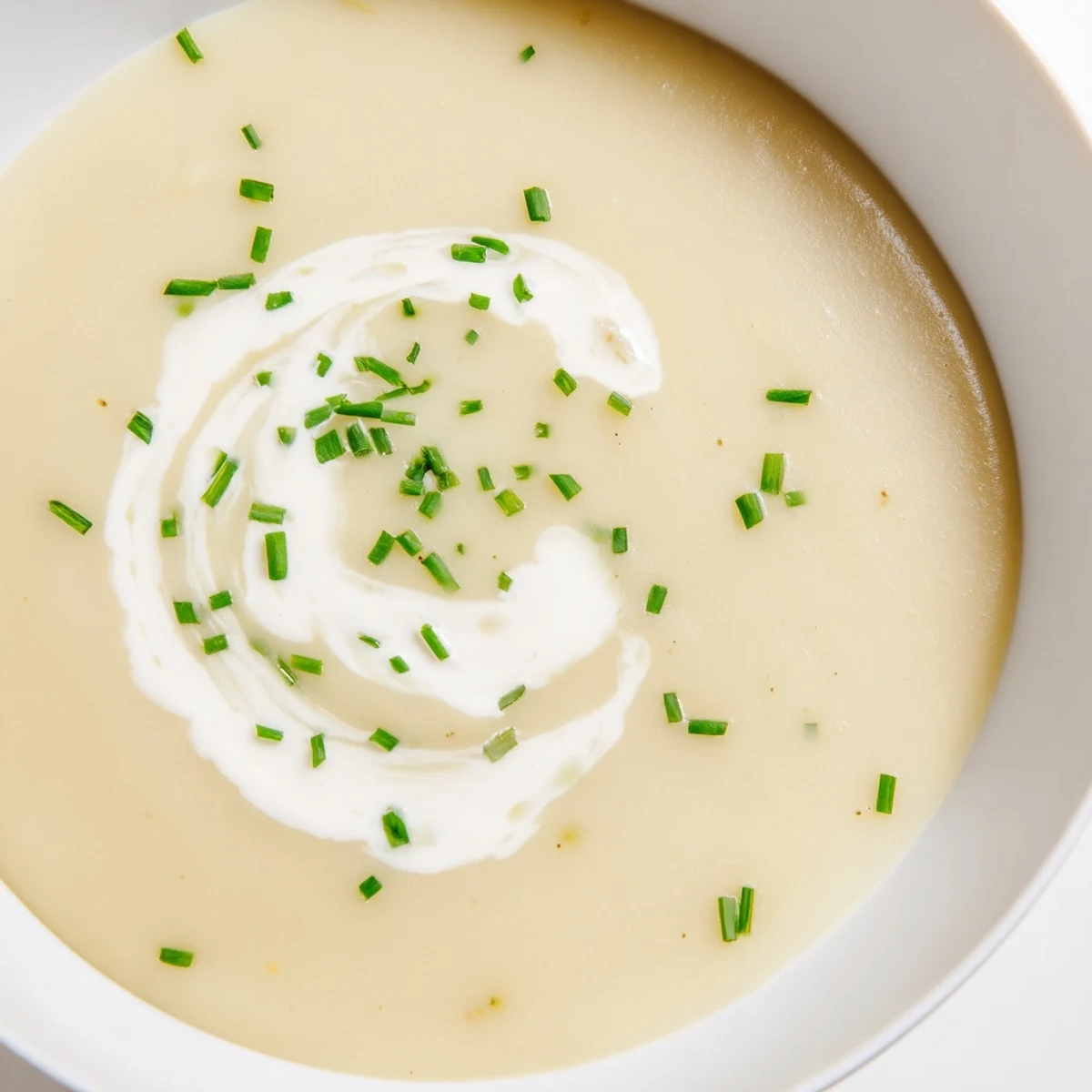 Creamy potato soup with chives in a rustic bowl, topped with fresh herbs and extra cream for garnish.