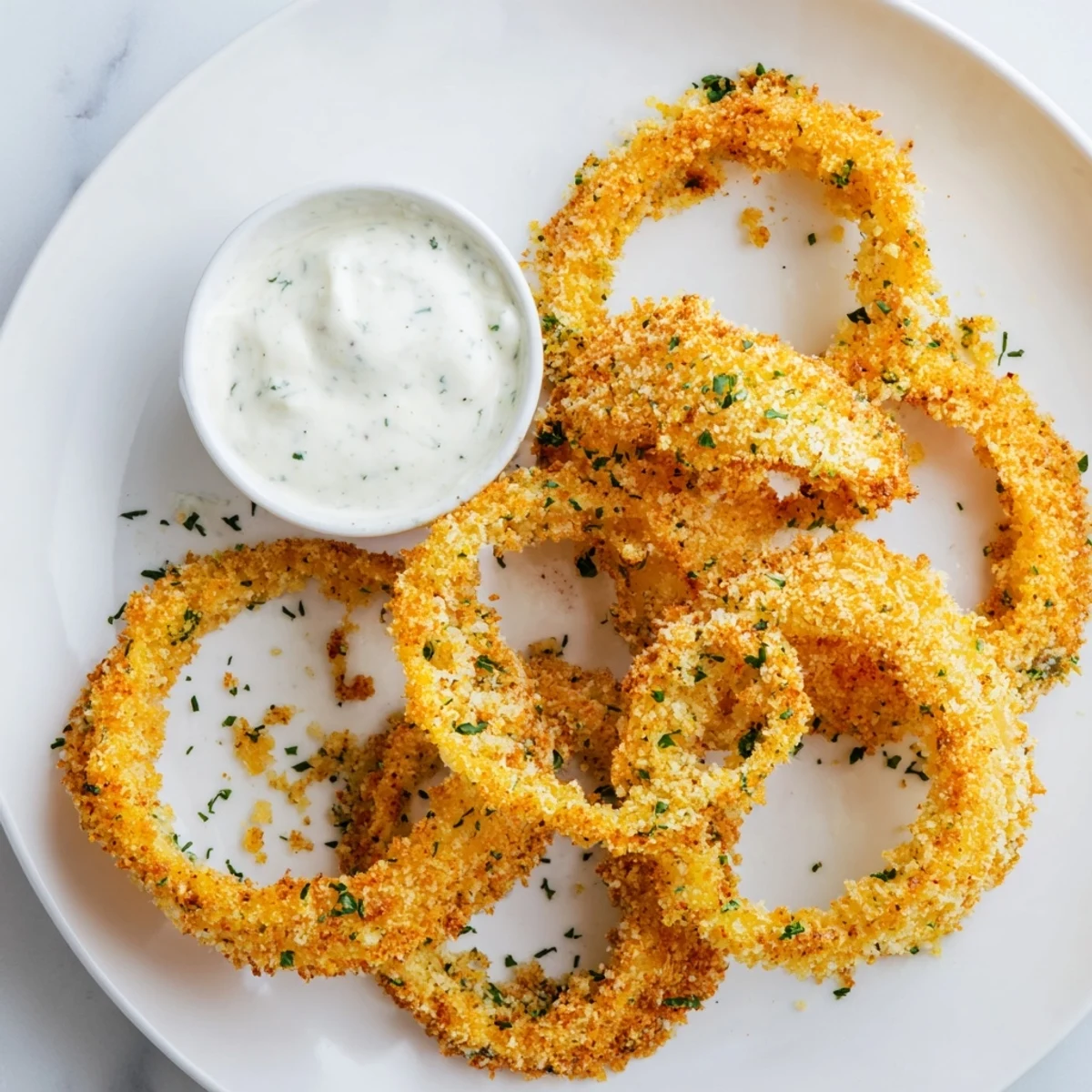 Crispy Baked Onion Rings with Ranch rest on a plate, showcasing golden breaded rings beside a bowl of cool homemade dip.