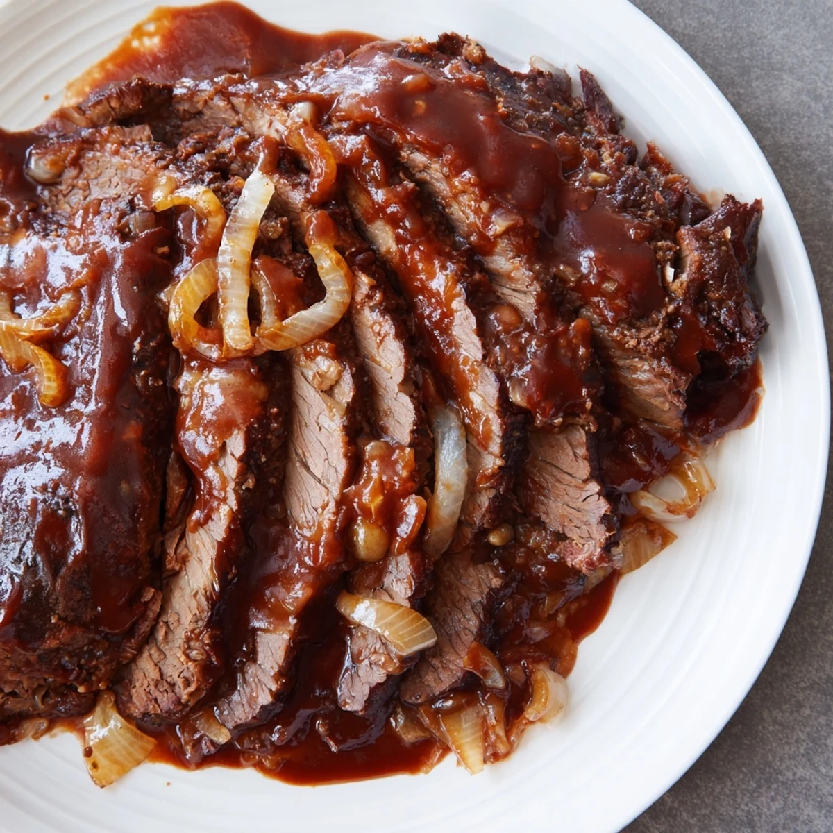 Homemade Slow Cooker Beef Brisket with BBQ Sauce resting on a cutting board with onions.