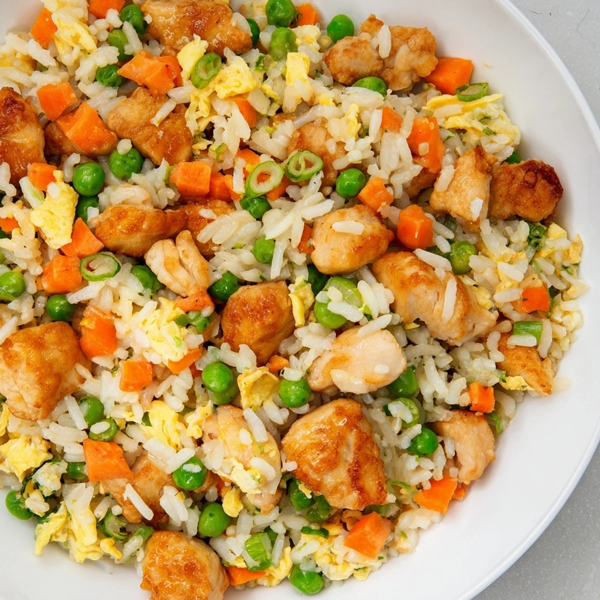 Close up on a spoonful of Chicken Fried Rice with Peas and Carrots next to chopsticks and soy sauce.