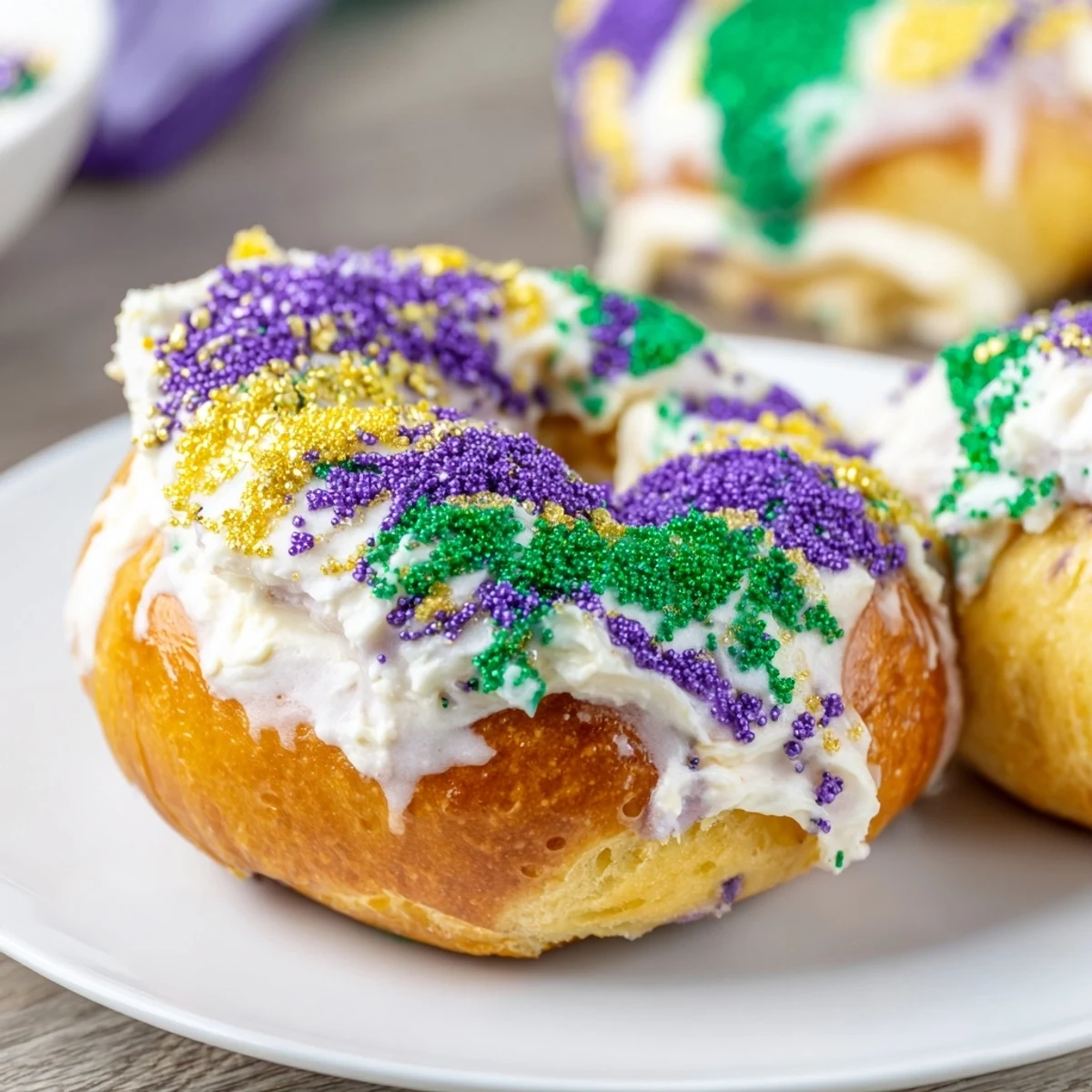 A close-up shows a Mardi Gras King Cake Bagel cut in half, revealing a thick swirl of sweet vanilla cream cheese filling.