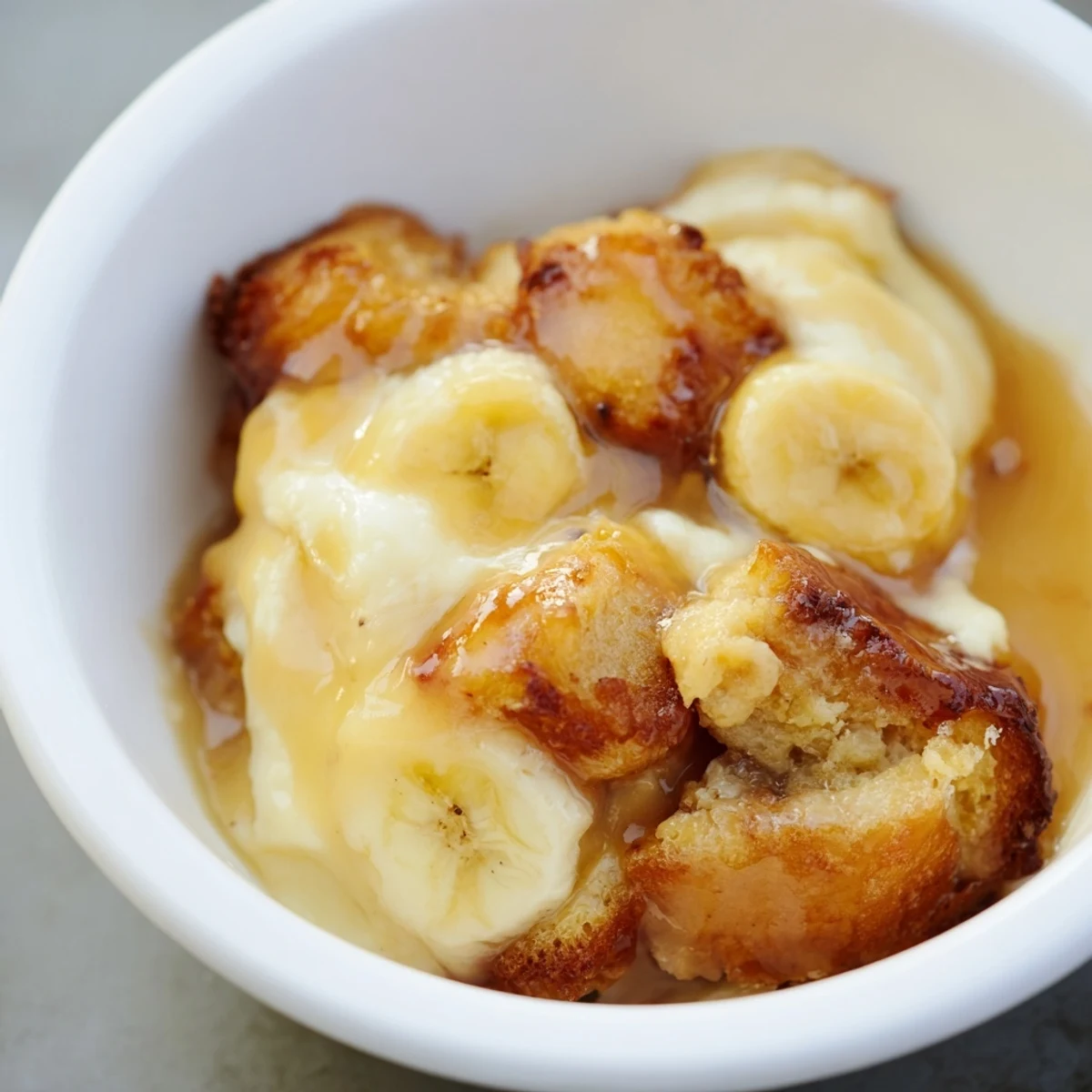 Creamy Bananas Foster Bread Pudding baked golden and topped with rich rum-butter caramel sauce and vanilla ice cream.