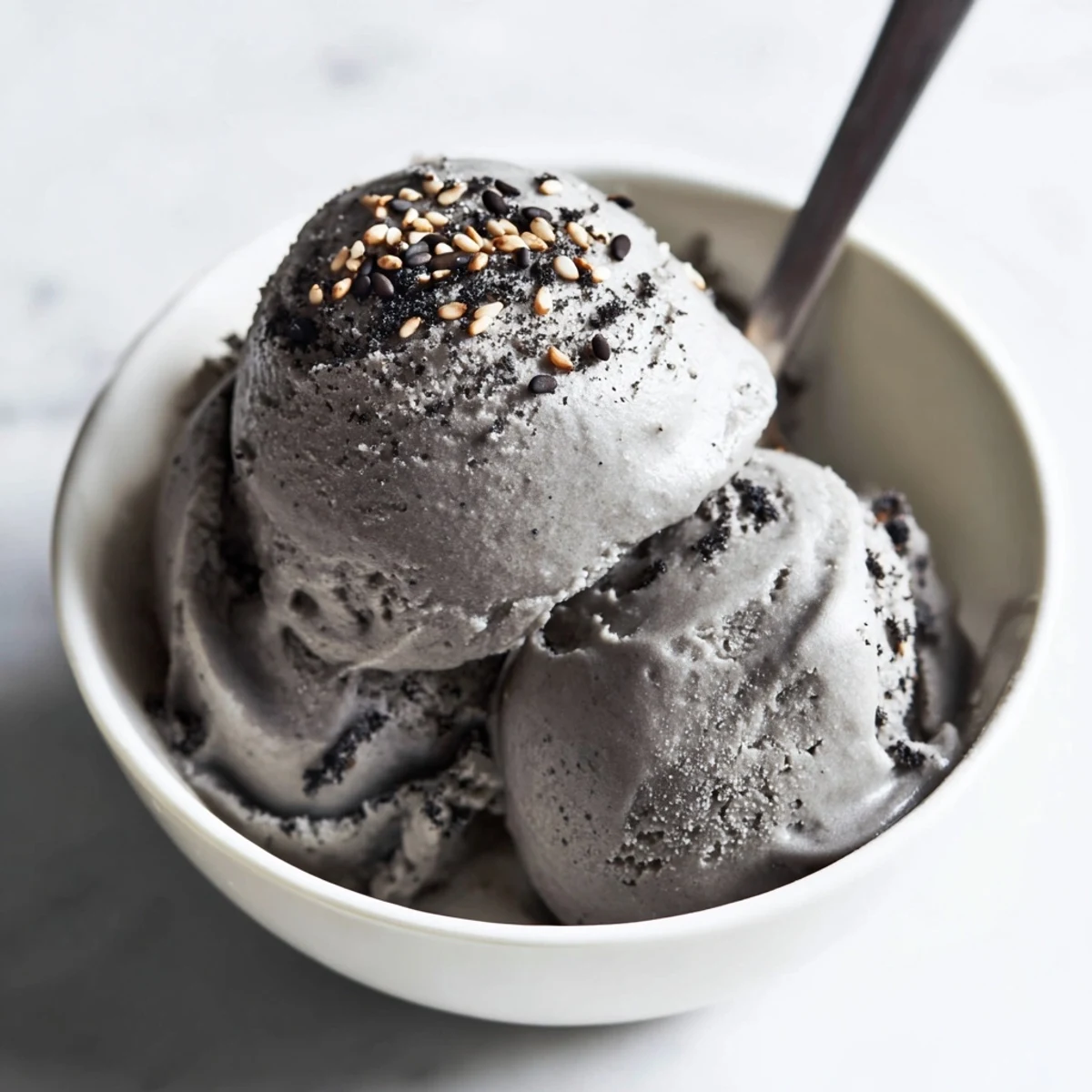 A scoop of toasted black sesame ice cream melting slightly on a waffle cone.