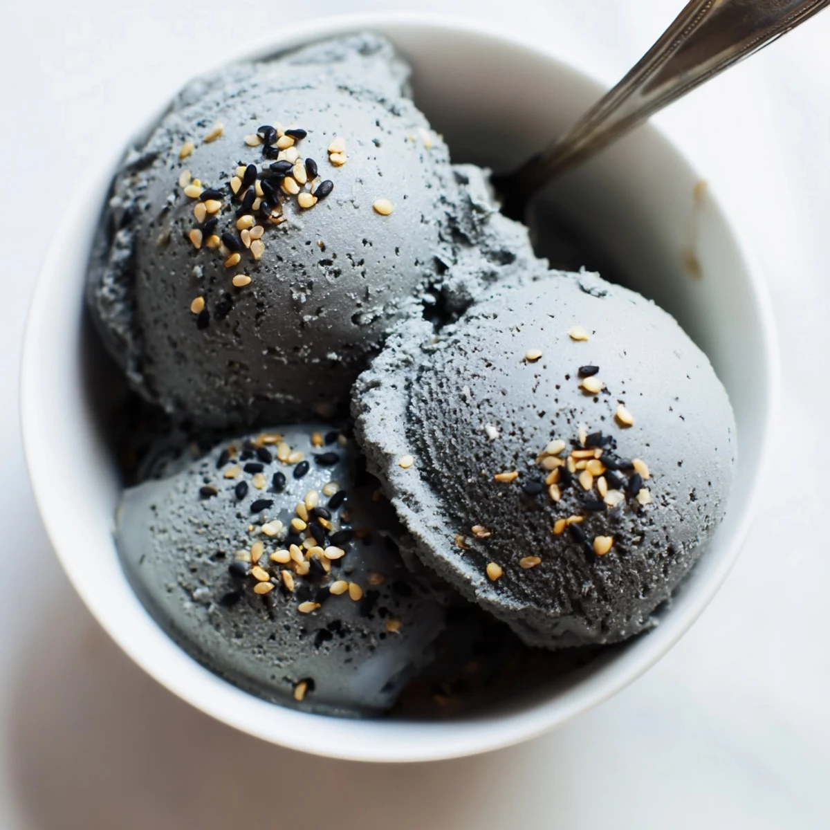 Creamy toasted black sesame ice cream in a clear bowl, topped with honey and sesame seeds.
