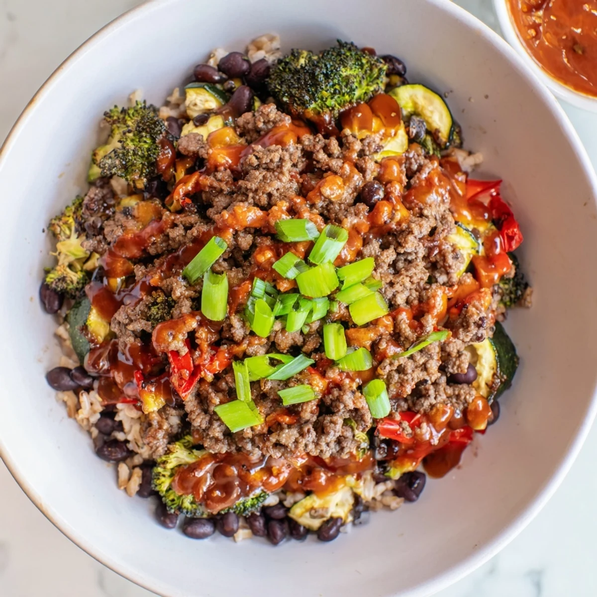 A vibrant meal prep bowl shows fluffy quinoa base, seasoned ground beef, and colorful veggies, finished with a sweet and spicy hot honey drizzle.