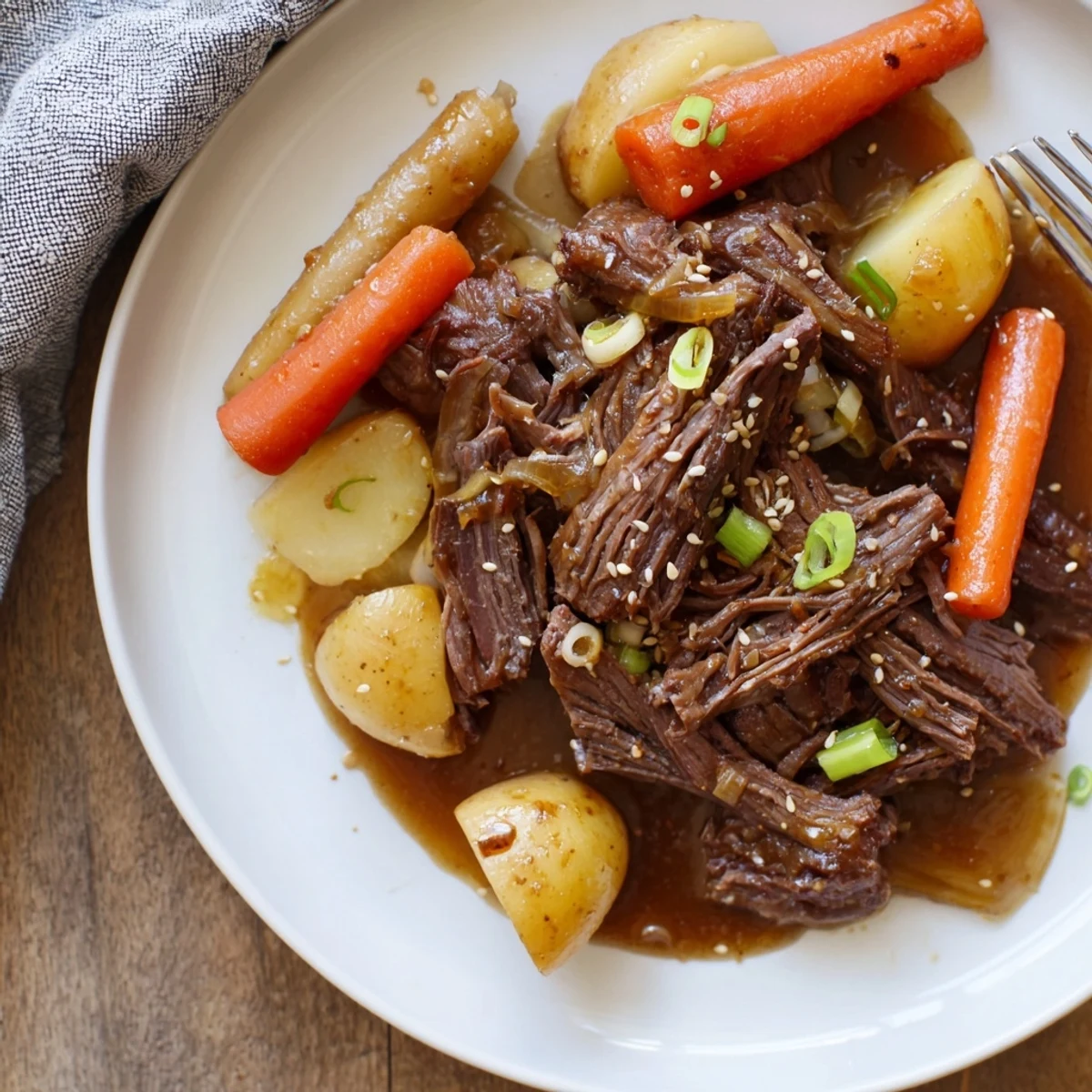 Fork-tender Slow Cooker Korean Beef Pot Roast With Soy Garlic Gravy drizzled over carrots and potatoes.