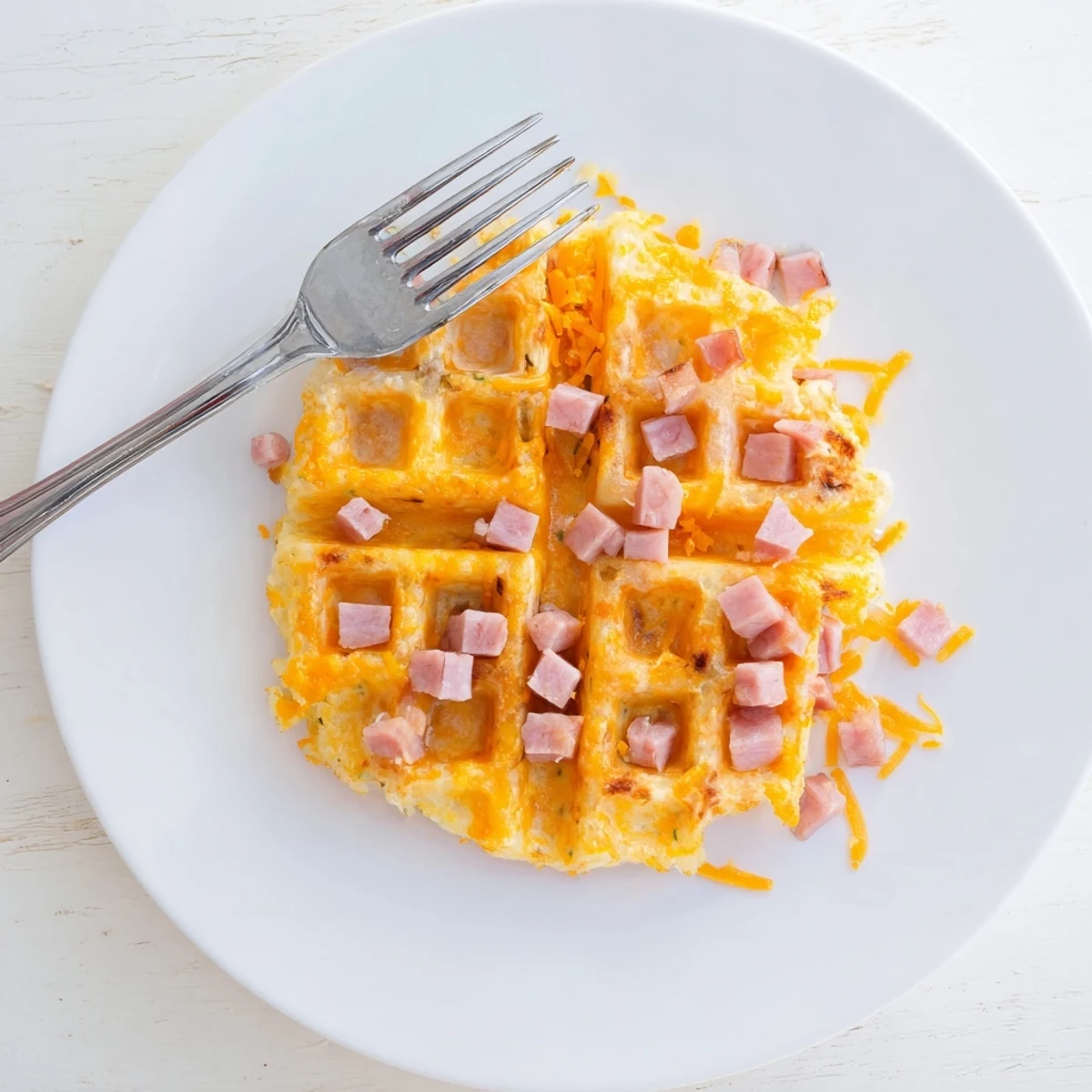 Golden crispy Ham and Cheese Chaffles with melted cheddar and diced ham, served warm on a plate for breakfast.