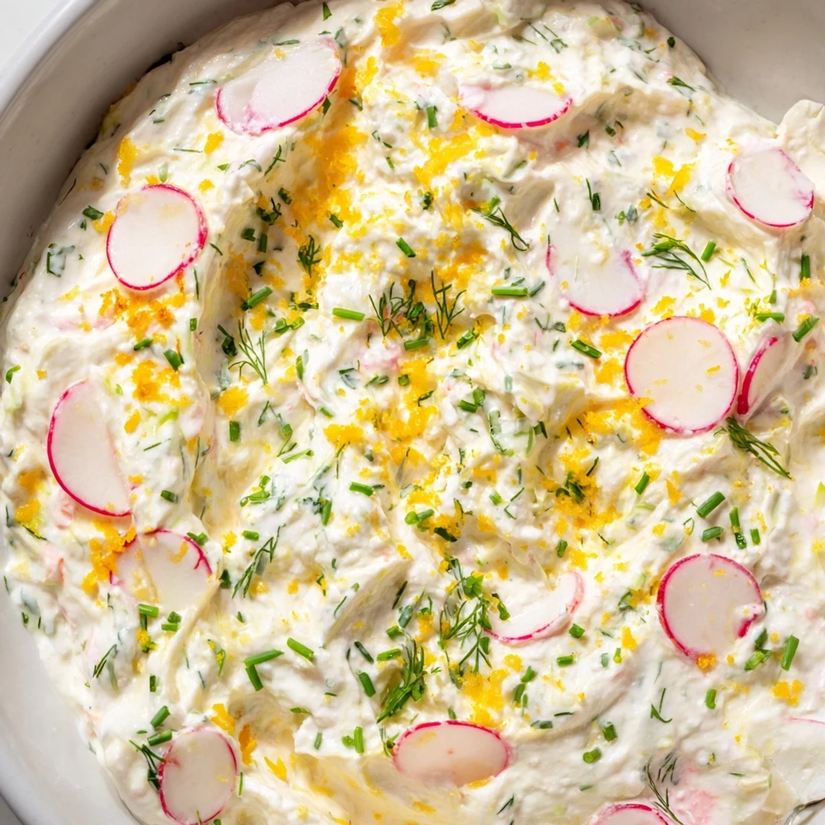 A close-up of creamy Simple Easter Herb Cheese Dip topped with fresh chives and dill, served with colorful vegetable sticks for dipping.