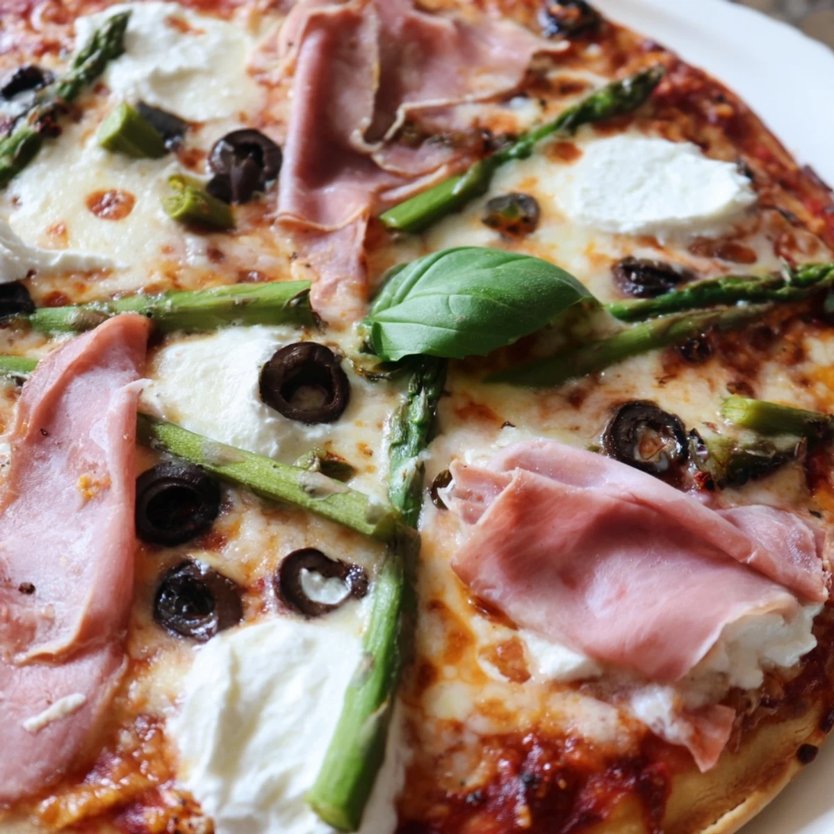 A close-up of a golden Ham, Olive, Asparagus, and Ricotta Pizza fresh from the oven, featuring smoky ham slices and creamy ricotta dollops.