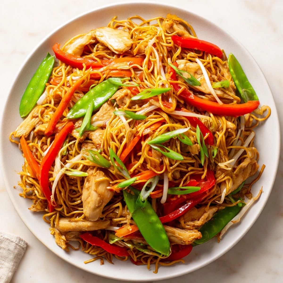 Plate of Chicken Chow Mein garnished with fresh scallions, ready to serve with a side of chili oil.
