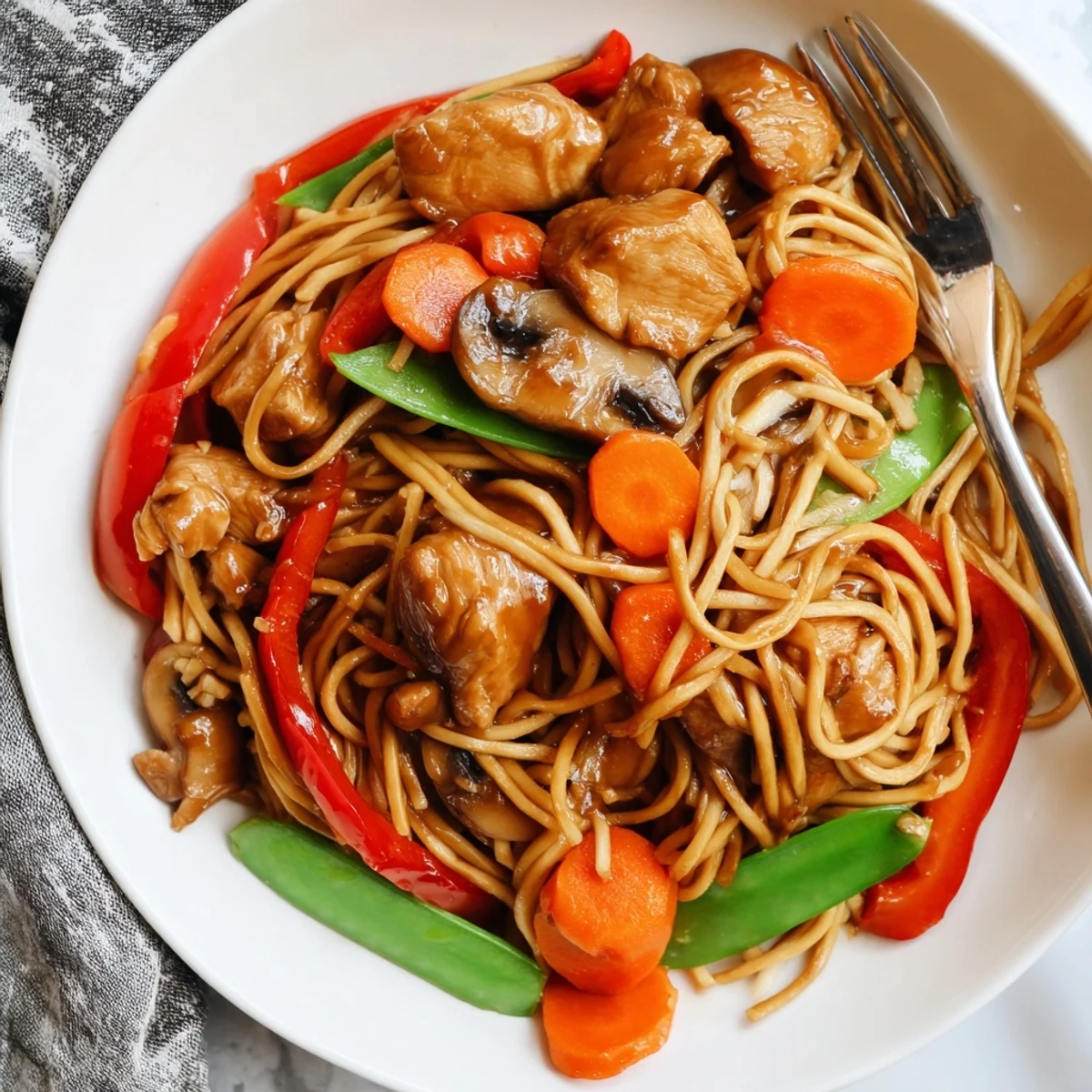 Crockpot chicken lo mein piled high with tender noodles, colorful bell peppers, and carrots in glossy brown sauce