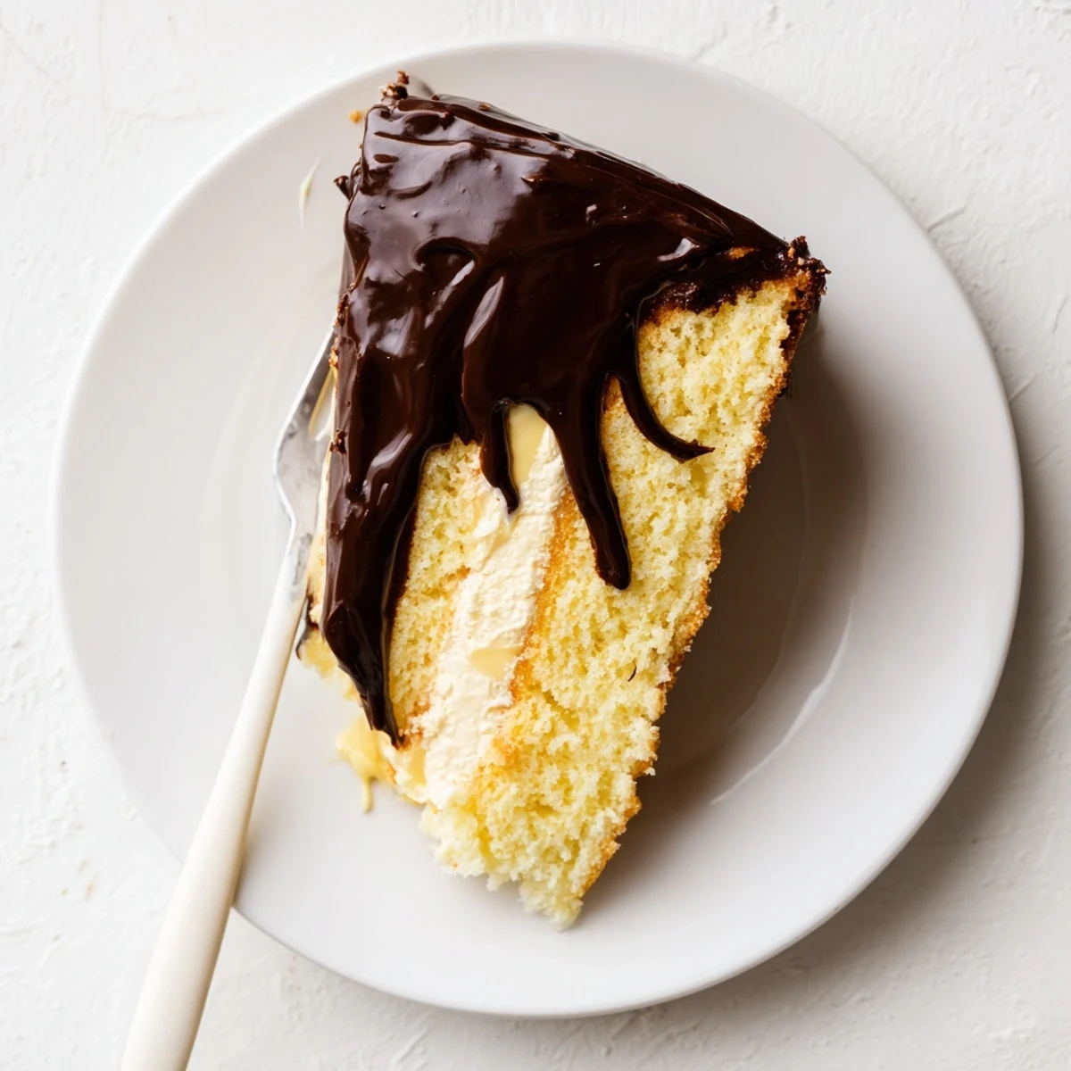 Homemade Boston Cream Pie featuring glossy chocolate topping over fluffy yellow cake and creamy pastry filling