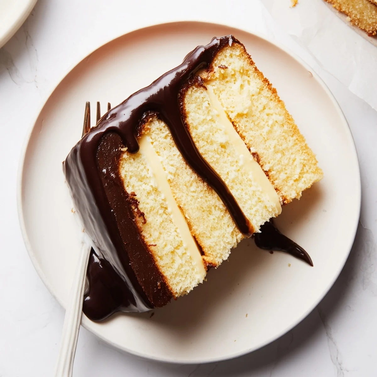 Decadent chocolate glazed Boston Cream Pie with rich cream filling on white serving plate