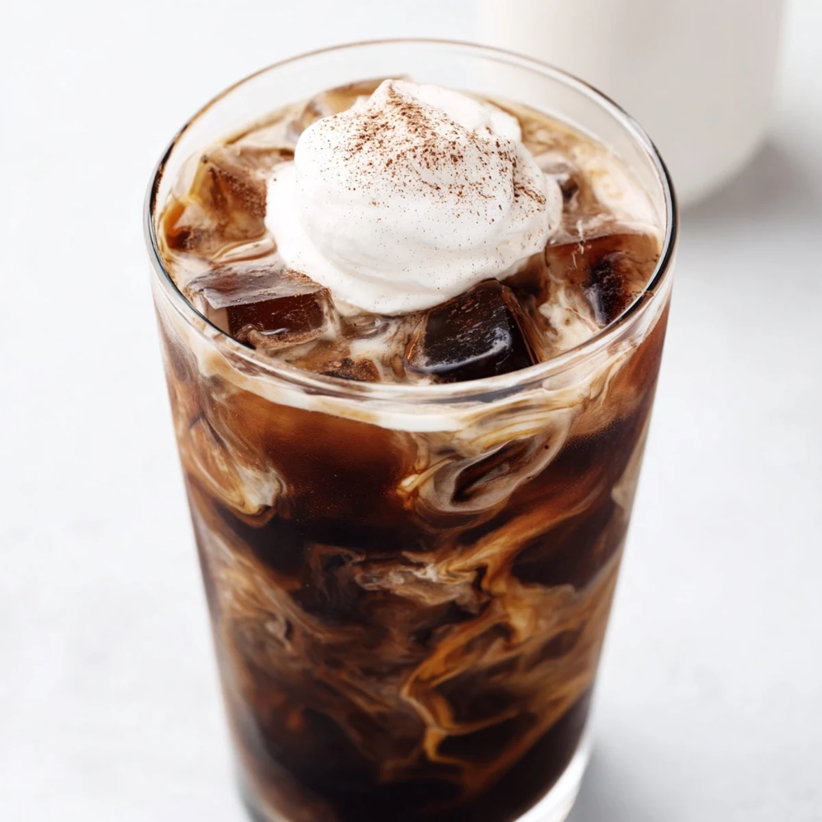 Tall chilled glass filled with refreshing iced coffee over ice cubes with cream