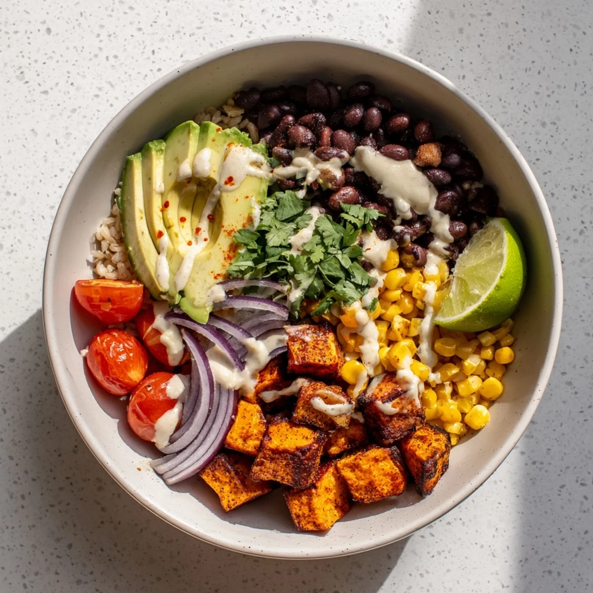 Colorful vegan sweet potato burrito bowl with roasted potatoes, black beans, avocado, fresh cilantro, and zesty lime rice