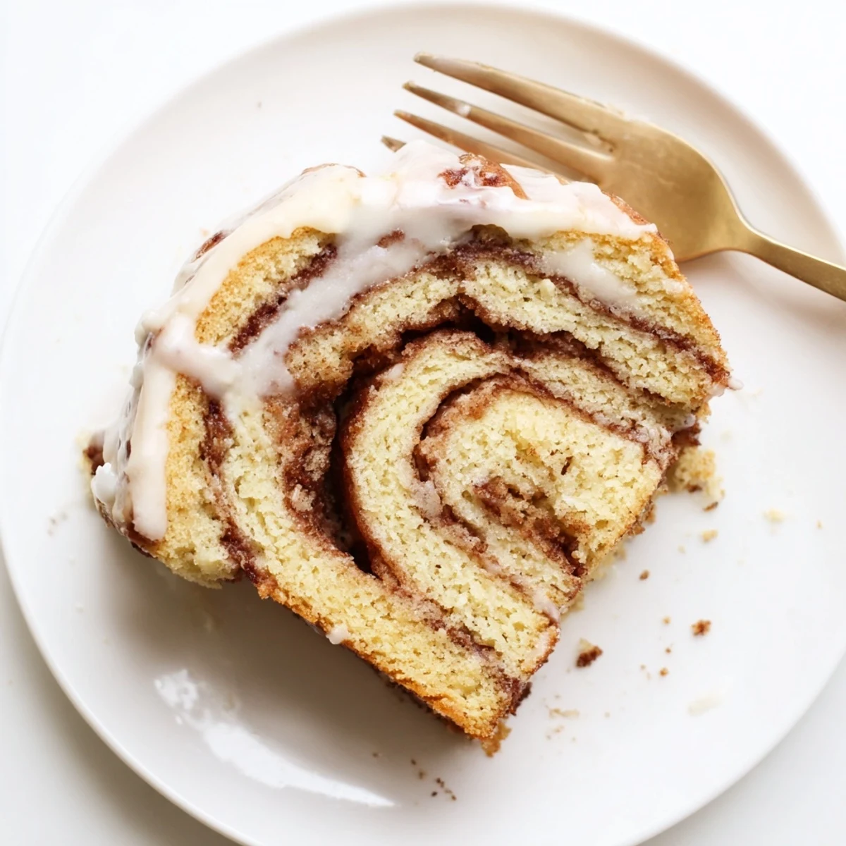 Warm swirled cinnamon roll cake served on a plate with powdered sugar glaze dripping down sides
