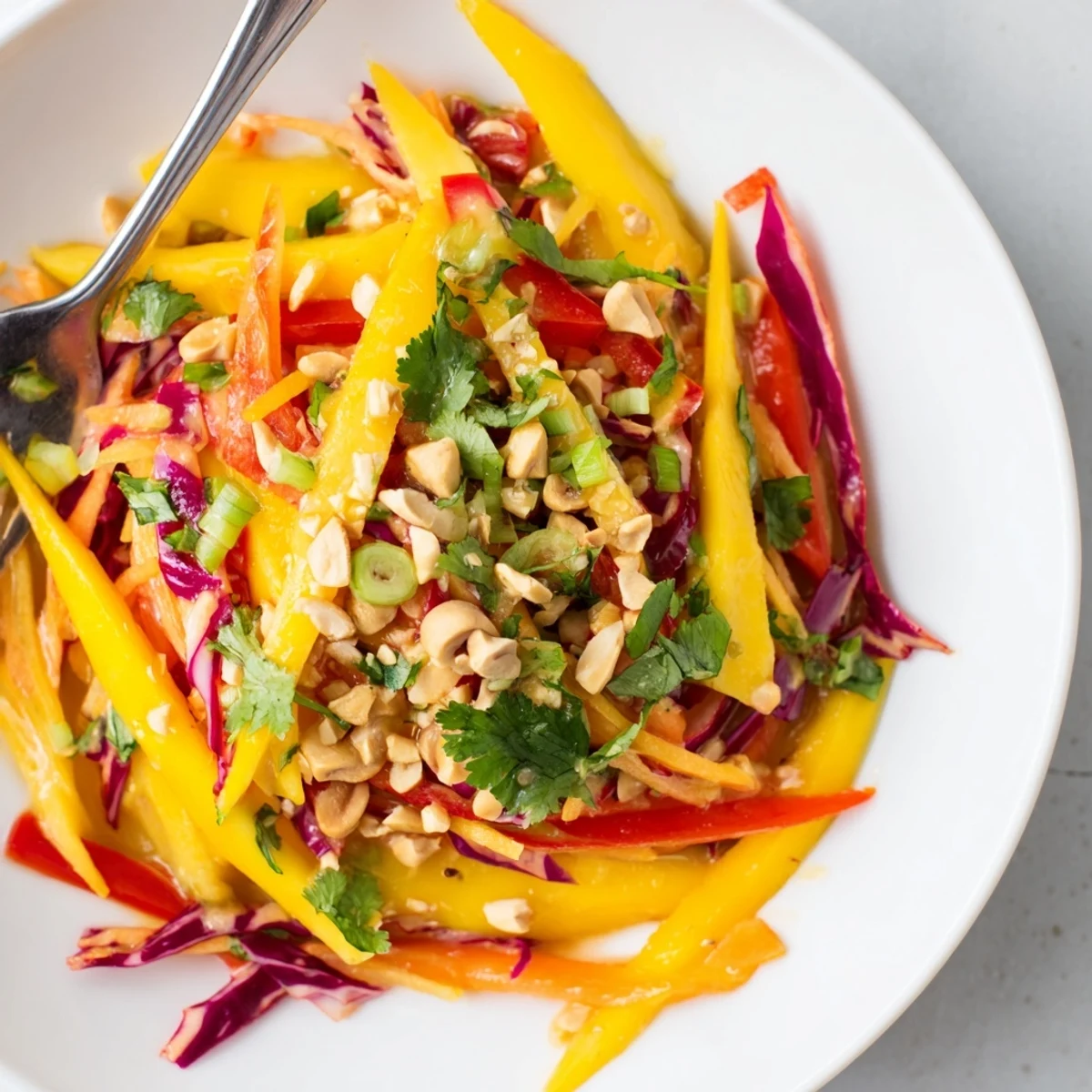 Vibrant mango slaw topped with toasted cashews and fresh cilantro on white plate