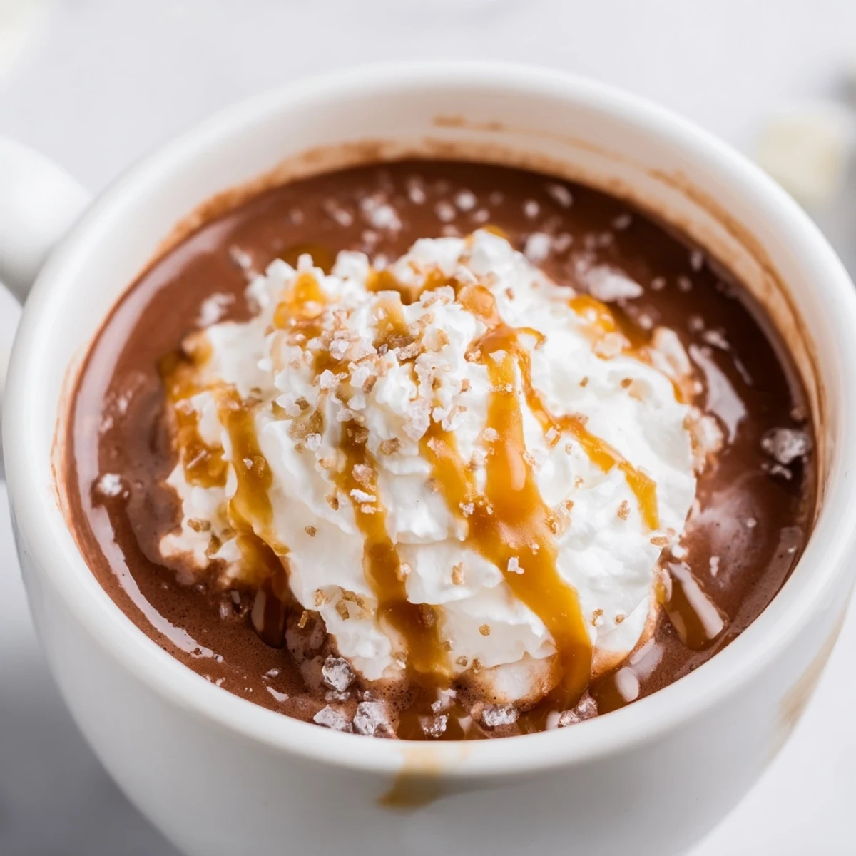 Rich chocolate salted caramel hot chocolate with sea salt garnish served in white ceramic mugs