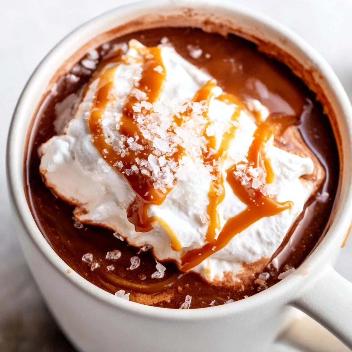 Steaming salted caramel hot chocolate with fluffy whipped cream topping and flaky sea salt sprinkle