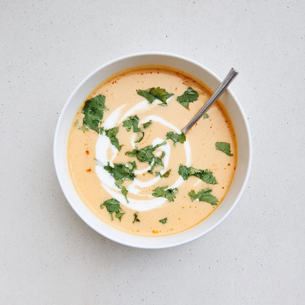 Creamy spicy apple soup garnished with fresh herbs and coconut cream swirl in white bowl