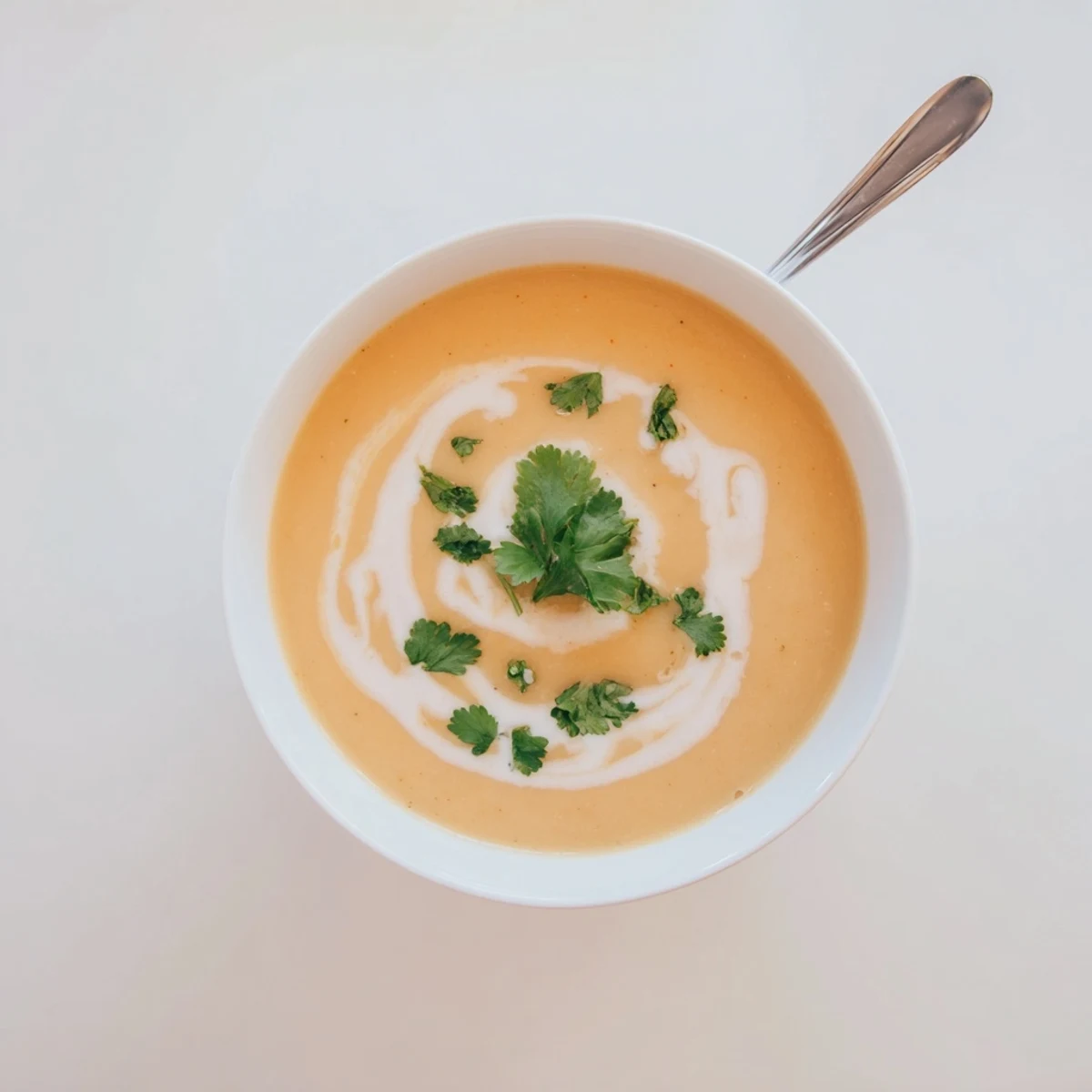 Steaming bowl of spicy apple soup with vibrant coconut cream and chopped coriander on rustic table