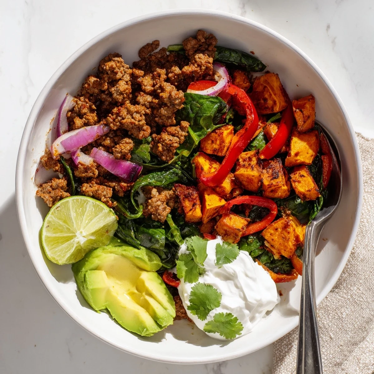 Steaming bowl of spiced ground beef and tender sweet potatoes garnished with creamy avocado, cilantro, and a dollop of Greek yogurt