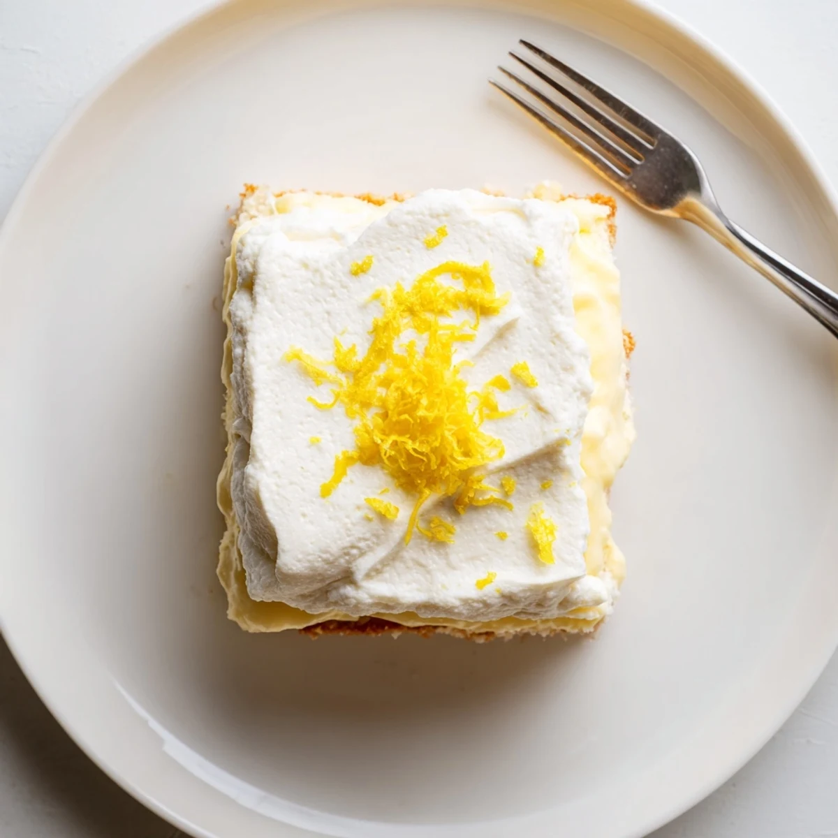 A bright Lemon Lush Cake garnished with lemon zest, served on plate