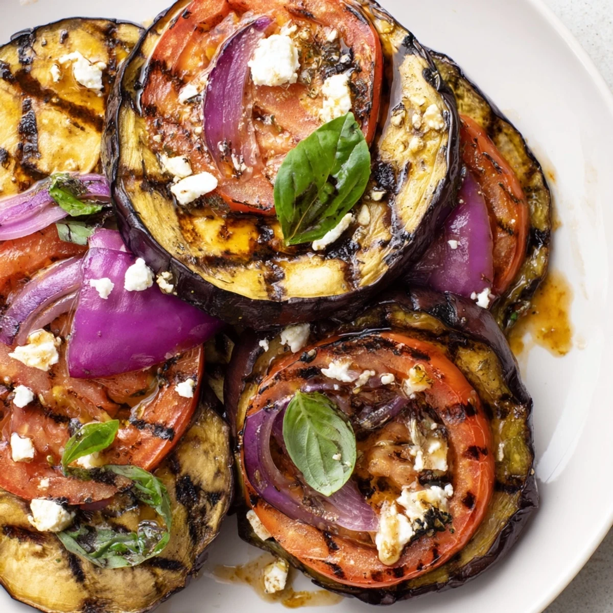 Charred grilled tomato eggplant layered with red onion and drizzled with balsamic marinade on a rustic plate