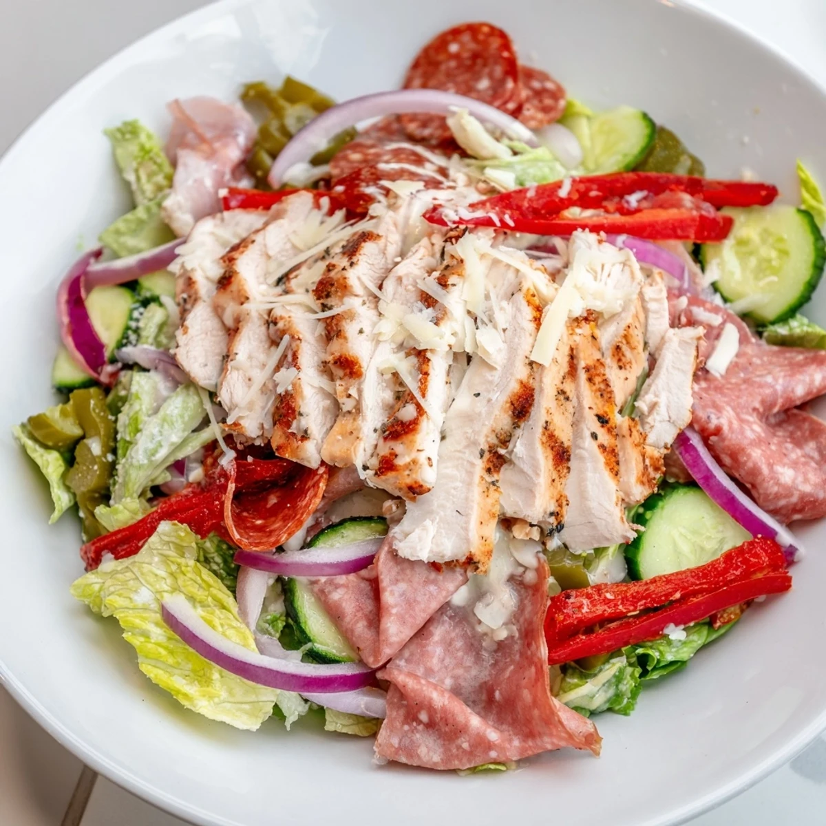 A colorful bowl of Italian Grinder Chicken Salad layered with sliced chicken, salami, provolone, and crisp veggies.  