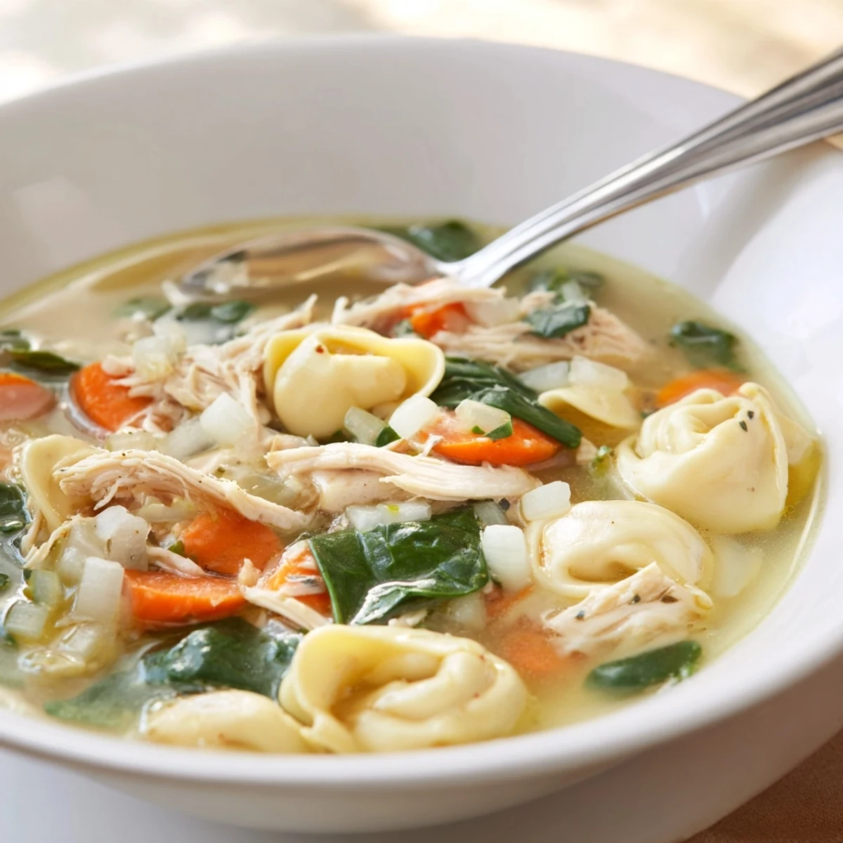 Creamy Crockpot Chicken Tortellini soup topped with parmesan cheese and fresh spinach.