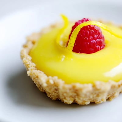 Creamy mini vegan lemon tarts in crisp almond crusts garnished with delicate lemon zest